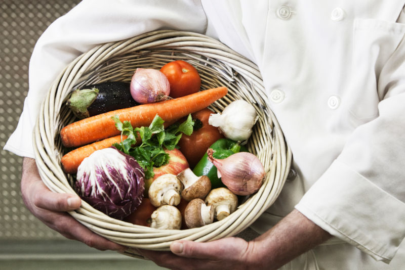 Chef holding a basket of freshly picked vegetables.